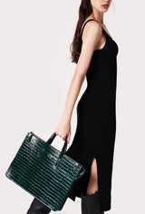A model carries a sophisticated green croco leather slim briefcase, showcasing its sophisticated design. The bag features a detachable shoulder strap, adding to its elegant appeal. The model confidently displays the bag's size and craftsmanship while exuding a sense of style and elegance.