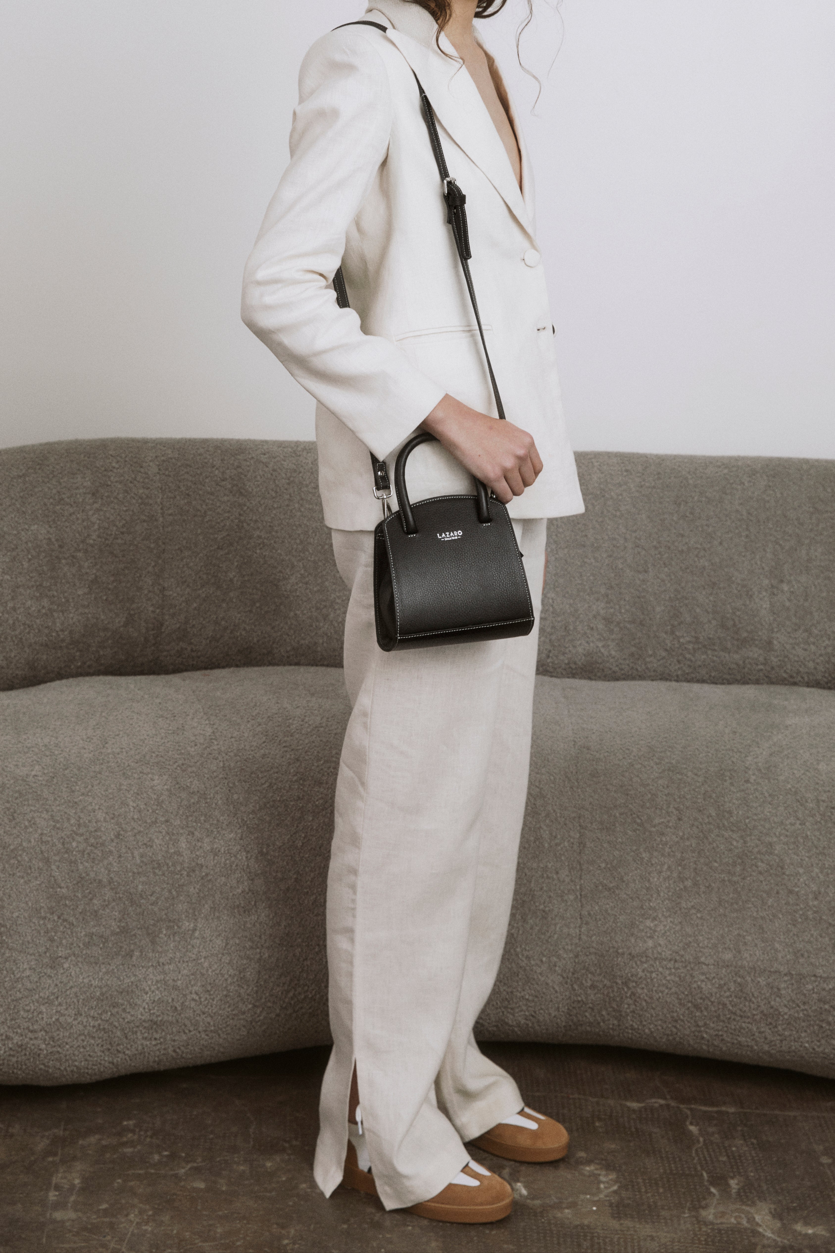 Woman in a white outfit holding a black handbag against a neutral background