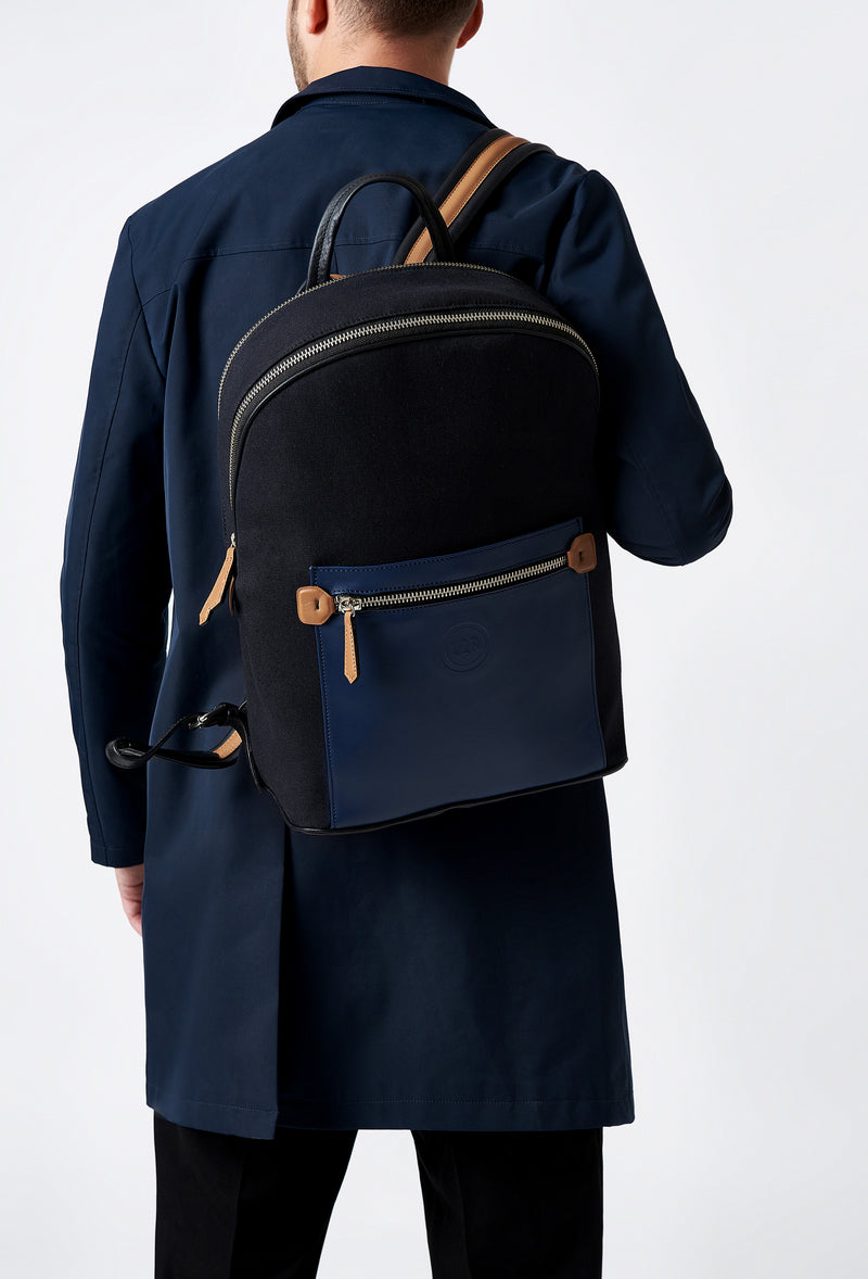 A model carries a sophisticated black canvas and leather backpack with laptop compartment, showcasing its sophisticated design. The bag features external and internal multifunctional zippered pockets, adding to its elegant appeal. The model confidently displays the bag's size and craftsmanship while exuding a sense of style and elegance.