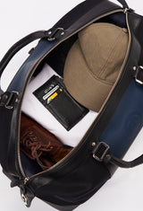 Interior of a Black Canvas and Leather Duffel Bag packed with a Lazaro cardholder, clothes, baseball cap and a pair of shoes.
