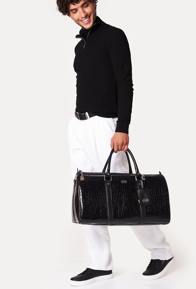 A model carries a sophisticated black croco leather duffel bag, showcasing its luxurious design. The bag features a lock closure, adding to its elegant appeal. The model confidently displays the bag's size and craftsmanship while exuding a sense of style and sophistication.