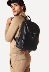 A model carries a sophisticated black leather backpack, showcasing its sophisticated design. The bag features unique needlework on its side, adding to its elegant appeal. The model confidently displays the bag's size and craftsmanship while exuding a sense of style and elegance.