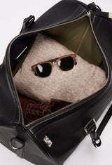 Interior of a Black Leather Duffel Bag with lock closure packed with clothes, sunglasses and a pair of shoes.