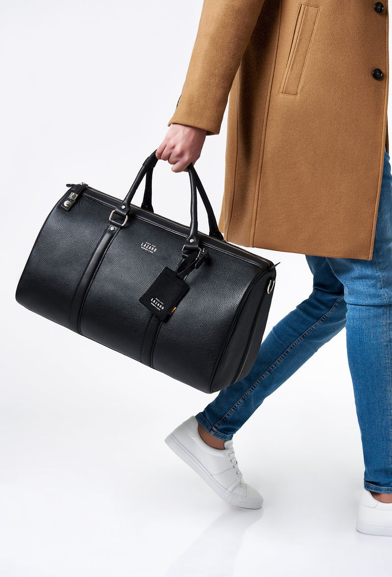 A model carries a sophisticated black leather duffel bag, showcasing its luxurious design. The bag features a lock closure, adding to its elegant appeal. The model confidently displays the bag's size and craftsmanship while exuding a sense of style and sophistication.