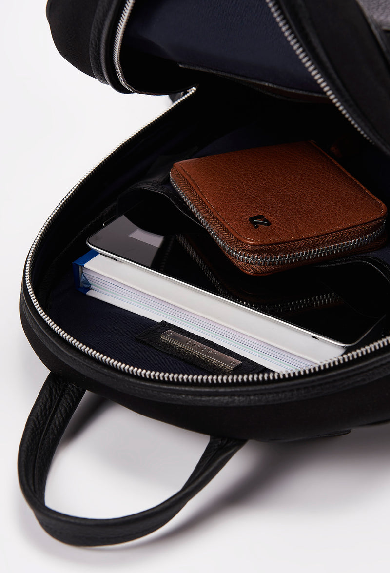 Interior of a Black Neoprene and Leather Backpack that shows a main compartment with a Lazaro wallet, a tablet and books..