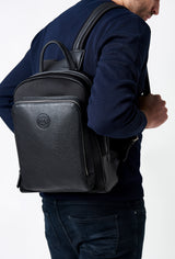 A model carries a sophisticated black neoprene and leather backpack, showcasing its sophisticated design. The bag features external and internal multifunctional zippered pockets, adding to its elegant appeal. The model confidently displays the bag's size and craftsmanship while exuding a sense of style and elegance.