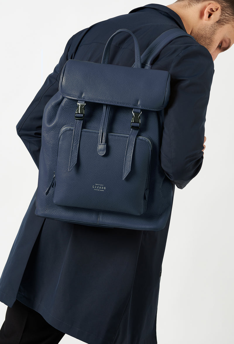 A model carries a sophisticated blue large leather backpack with buckle closure, showcasing its sophisticated design. The bag features external and internal multifunctional zippered pockets, adding to its elegant appeal. The model confidently displays the bag's size and craftsmanship while exuding a sense of style and elegance.