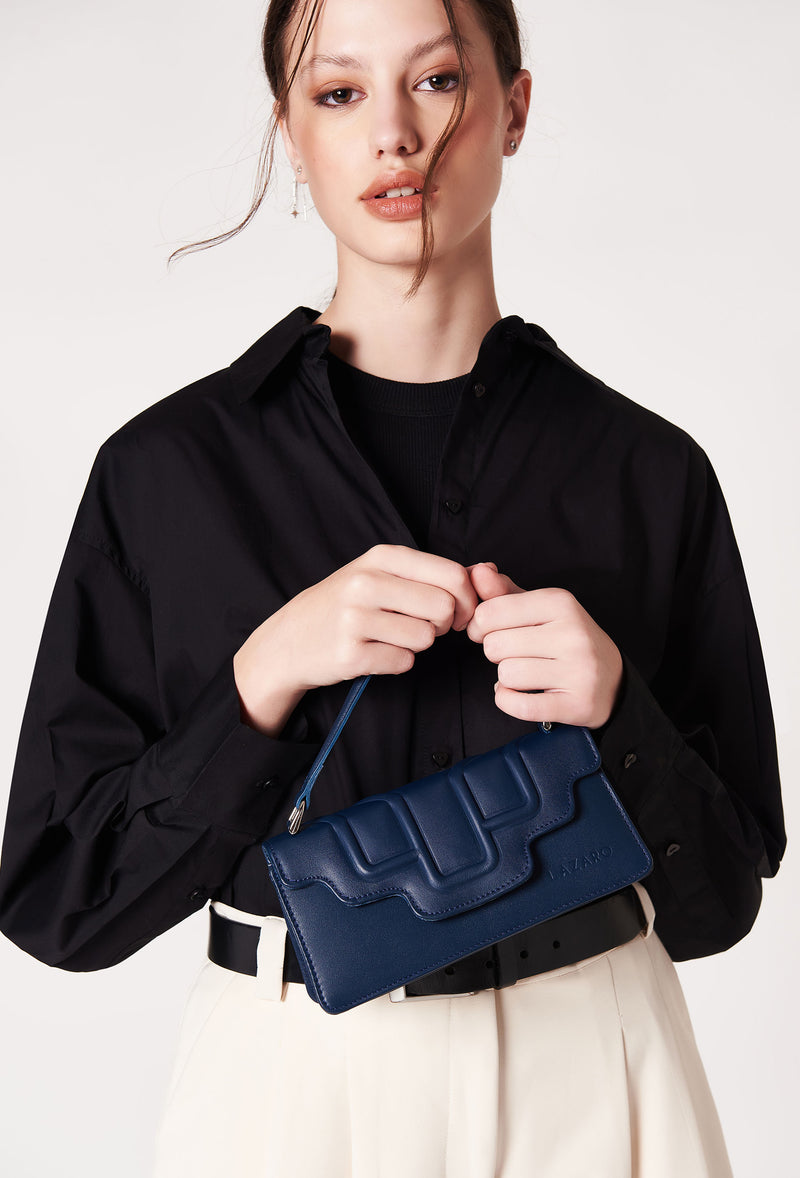 A model carries a sophisticated blue leather crossbody flap bag hilda, showcasing its sophisticated design. The bag features a raised design flap, adding to its elegant appeal. The model confidently displays the bag's size and craftsmanship while exuding a sense of style and elegance.