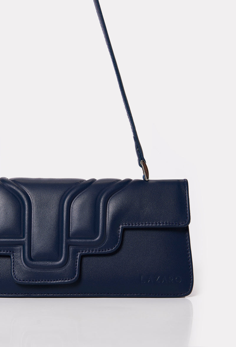 Partial photo of a Blue Leather Shoulder Flap Bag Hilda with a raised design flap and Lazaro logo.