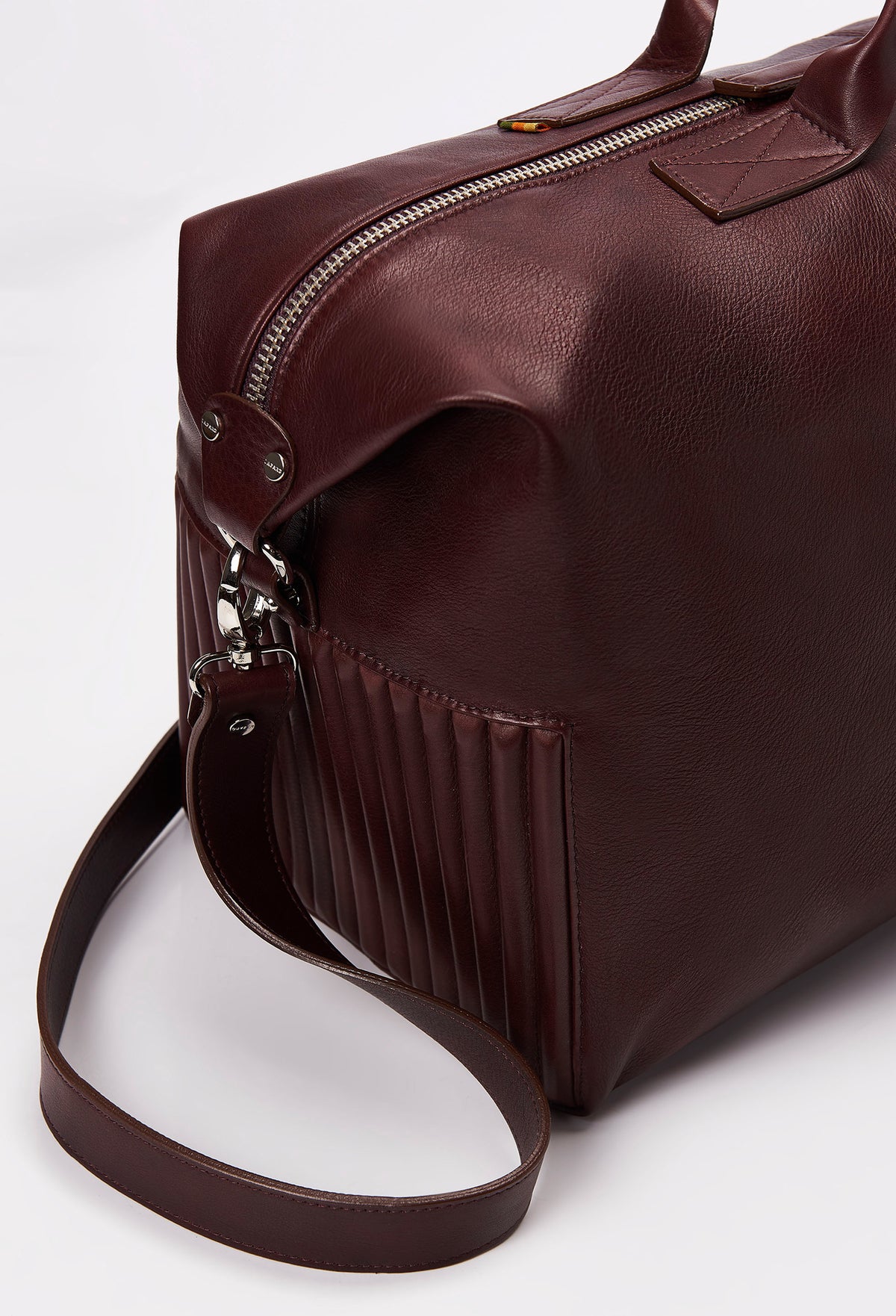 Partial photo of a Coffee Leather Duffel Bag with needlework on the sides, a zippered main compartment, and a detachable leather shoulder strap.