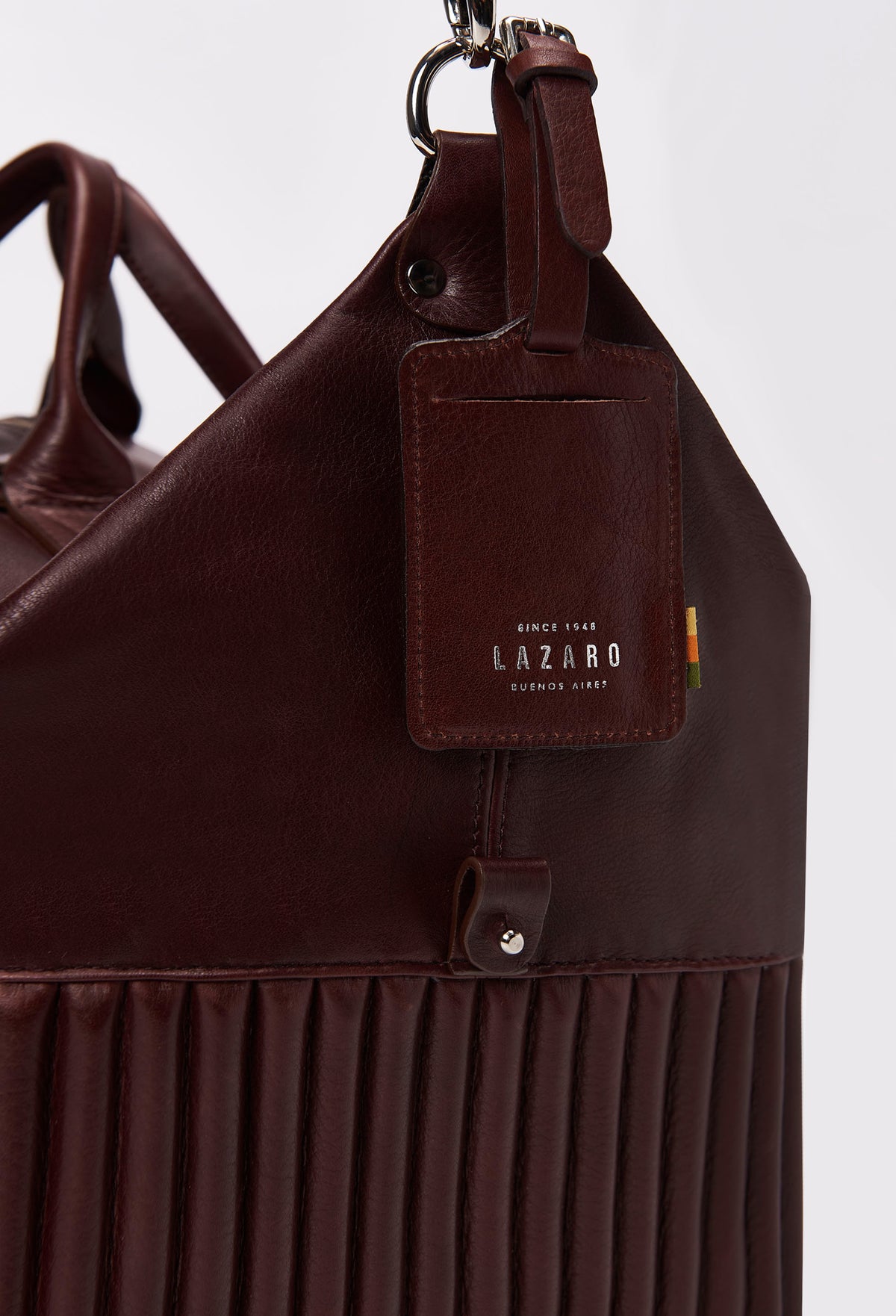 Partial photo of a Coffee Leather Duffel Bag with unique needlework on the side, a leather id tag and silver ironwork.