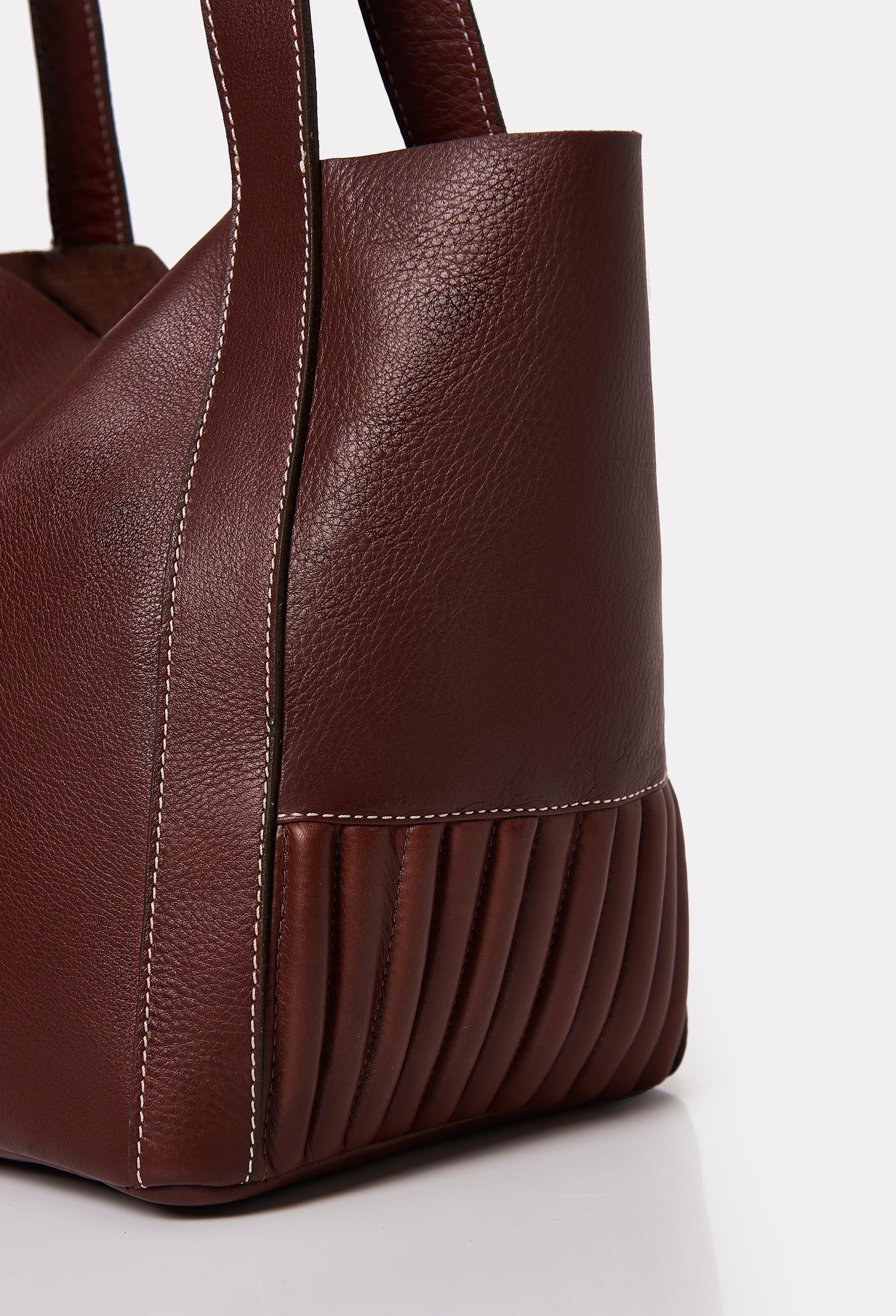 Partial photo of a Coffee Leather Small Bucket Bag Ushuaia with needlework on the sides and contrast stitching highlights.