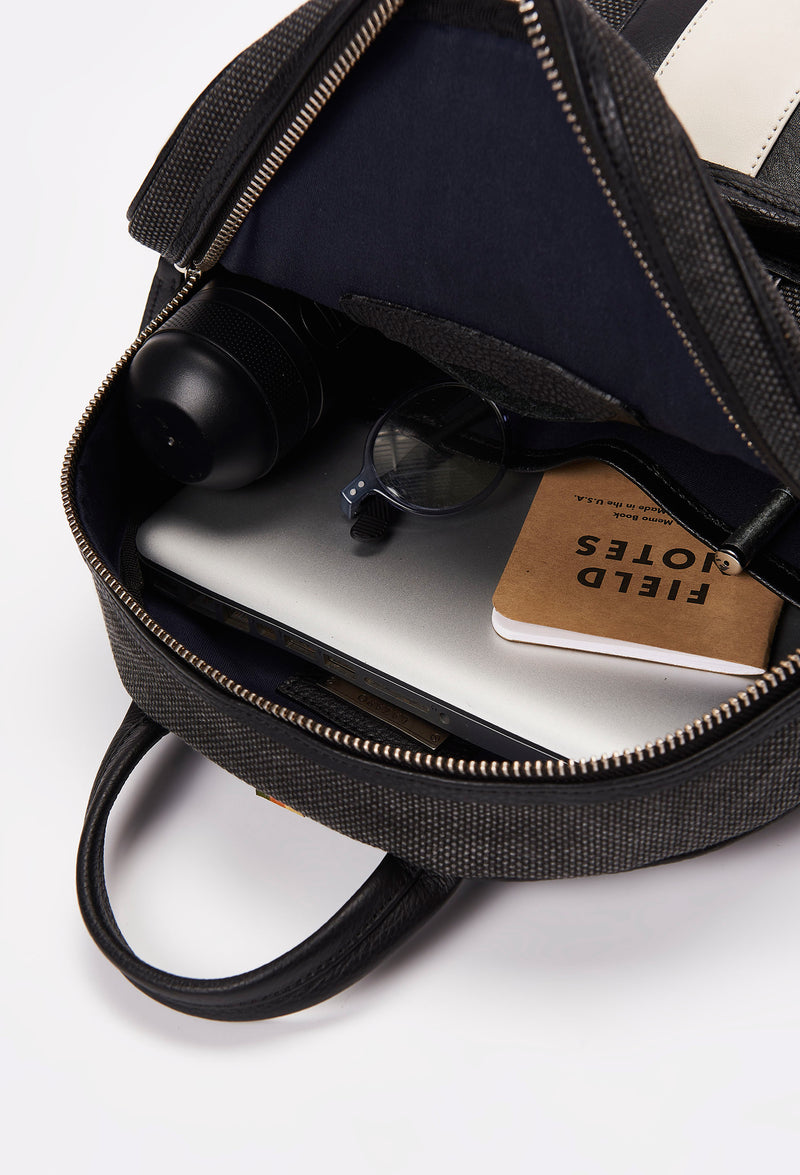 Interior of a Lightweight Canvas Zipper Backpack that shows a zippered main compartment and an internal cell phone pocket packed with a computer, a water bottle, glasses and a notebook.