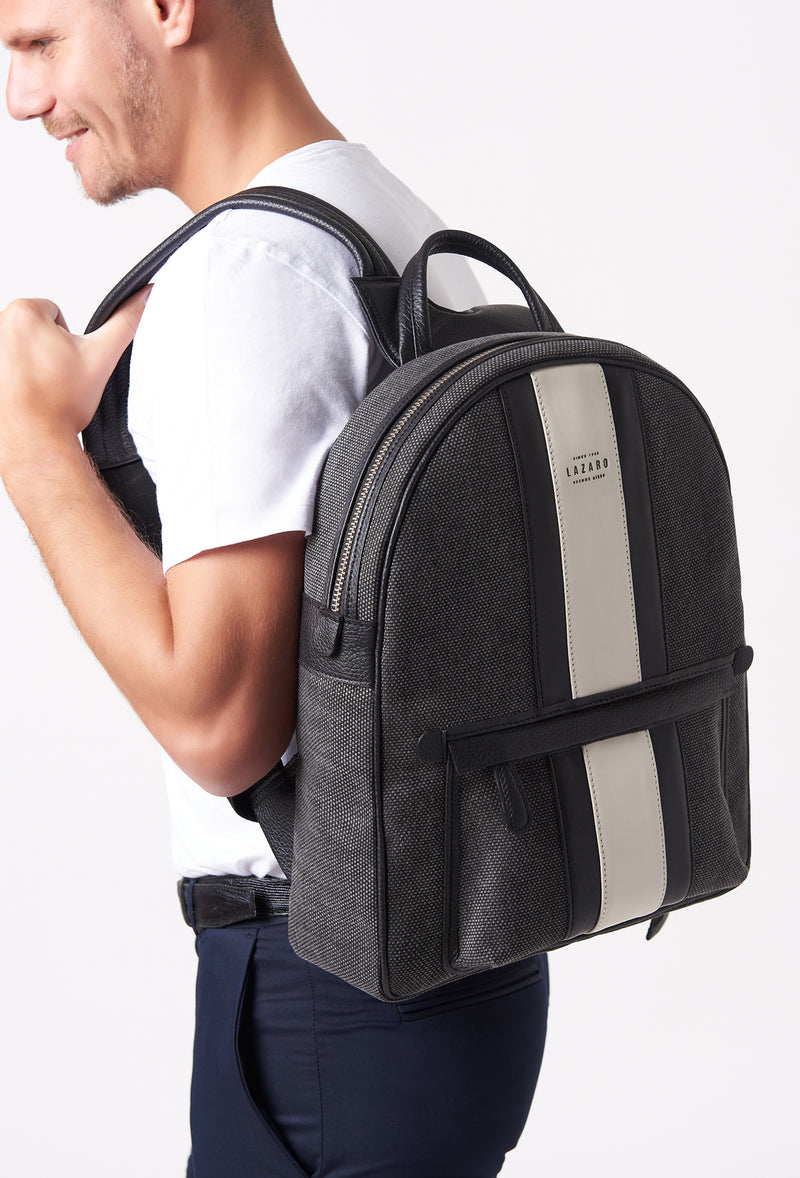 A model carries a sophisticated lightweight canvas backpack, showcasing its sophisticated design. The bag features leather trims in black and off white, external and internal multifunctional zippered pockets, adding to its elegant appeal. The model confidently displays the bag's size and craftsmanship while exuding a sense of style and elegance.