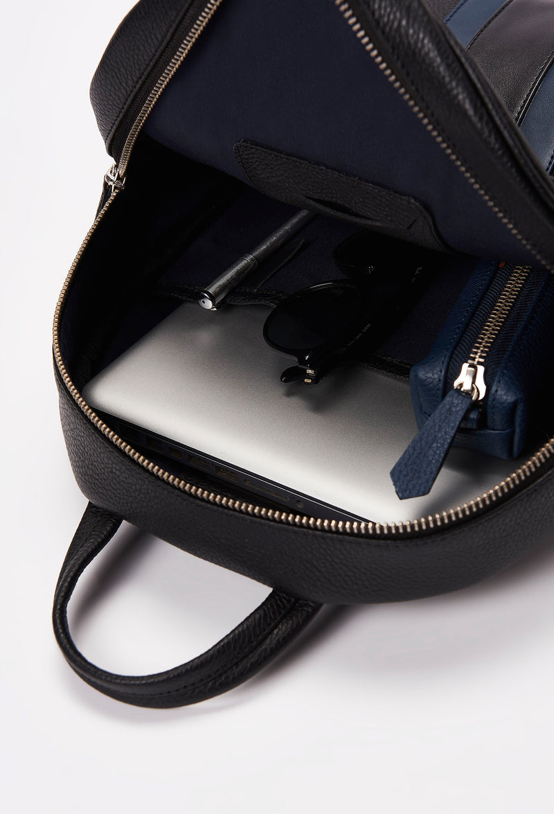 Interior of a Black Lightweight Leather Zipper Backpack that shows a zippered main compartment and an internal cell phone pocket packed with a computer, a Lazaro leather pencil case, sunglasses and a pen.