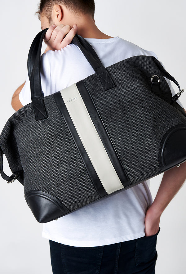 A model carries a sophisticated off white large canvas duffel bag, showcasing its luxurious design. The bag features leather stripes on the front, adding to its elegant appeal. The model confidently displays the bag's size and craftsmanship while exuding a sense of style and sophistication.