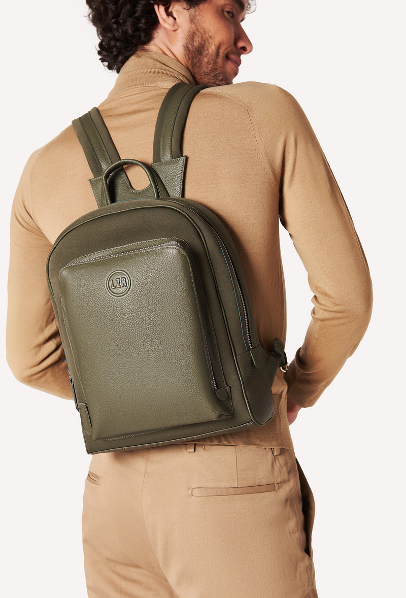 A model carries a sophisticated olive neoprene and leather backpack, showcasing its sophisticated design. The bag features external and internal multifunctional zippered pockets, adding to its elegant appeal. The model confidently displays the bag's size and craftsmanship while exuding a sense of style and elegance.