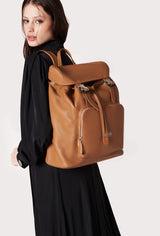 A model carries a sophisticated tan large leather backpack with buckle closure, showcasing its sophisticated design. The bag features external and internal multifunctional zippered pockets, adding to its elegant appeal. The model confidently displays the bag's size and craftsmanship while exuding a sense of style and elegance.