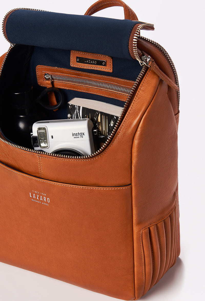 Interior of a Tan Leather Backpack that shows a zippered main compartment, the side needlework, a front pocket and an internal zippered pocket.