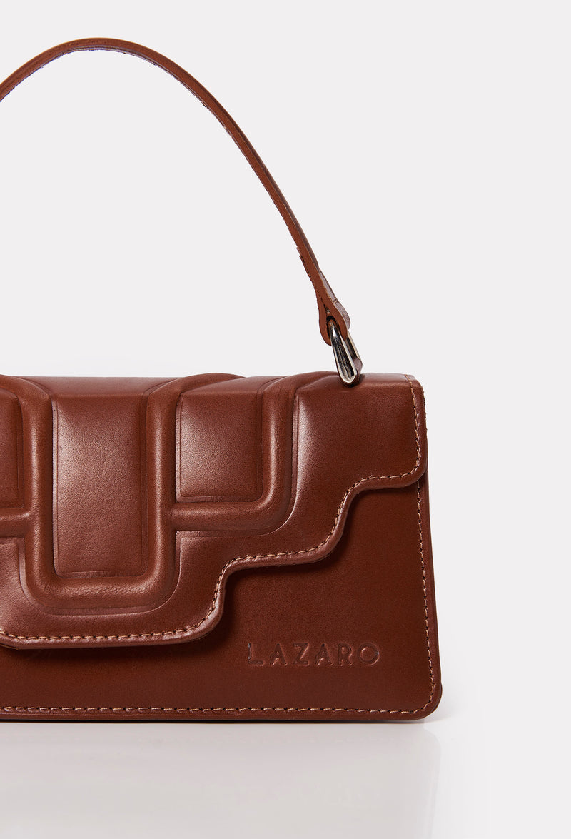 Partial photo of a Tan Leather Crossbody Flap Bag Hilda with a raised design flap and Lazaro logo.