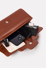 Interior of a Tan Leather Shoulder Flap Bag Hilda that shows the bag packed with a Lazaro card holder, cell phone, sunglasses, perfume, notebook and car keys.