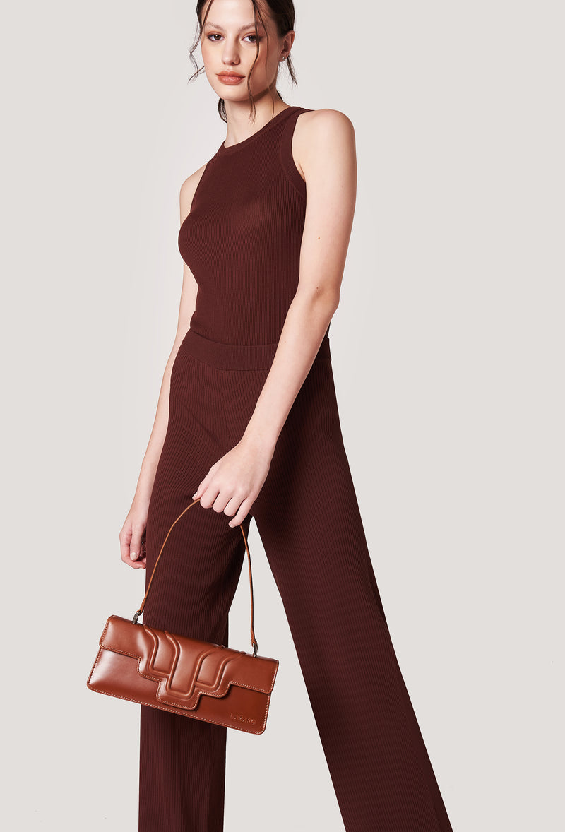 A model carries a sophisticated tan leather shoulder flap bag hilda, showcasing its sophisticated design. The bag features a raised design flap, adding to its elegant appeal. The model confidently displays the bag's size and craftsmanship while exuding a sense of style and elegance.