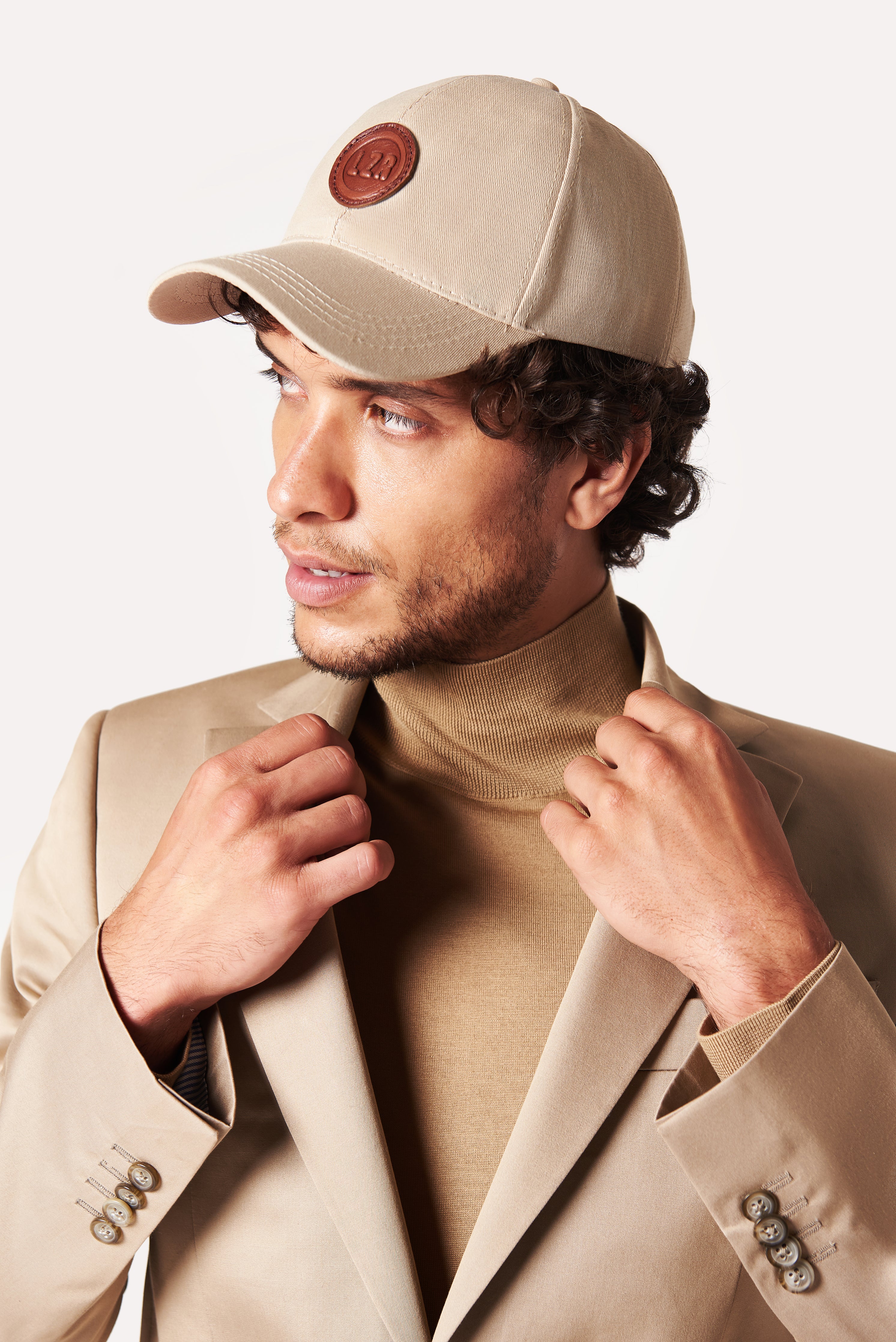 A model wears a Beige Baseball Cap with a Patched Leather Lazaro Logo and a leather adjustable strap. The model confidently displays the cap's size and craftsmanship while exuding a sense of style and elegance.