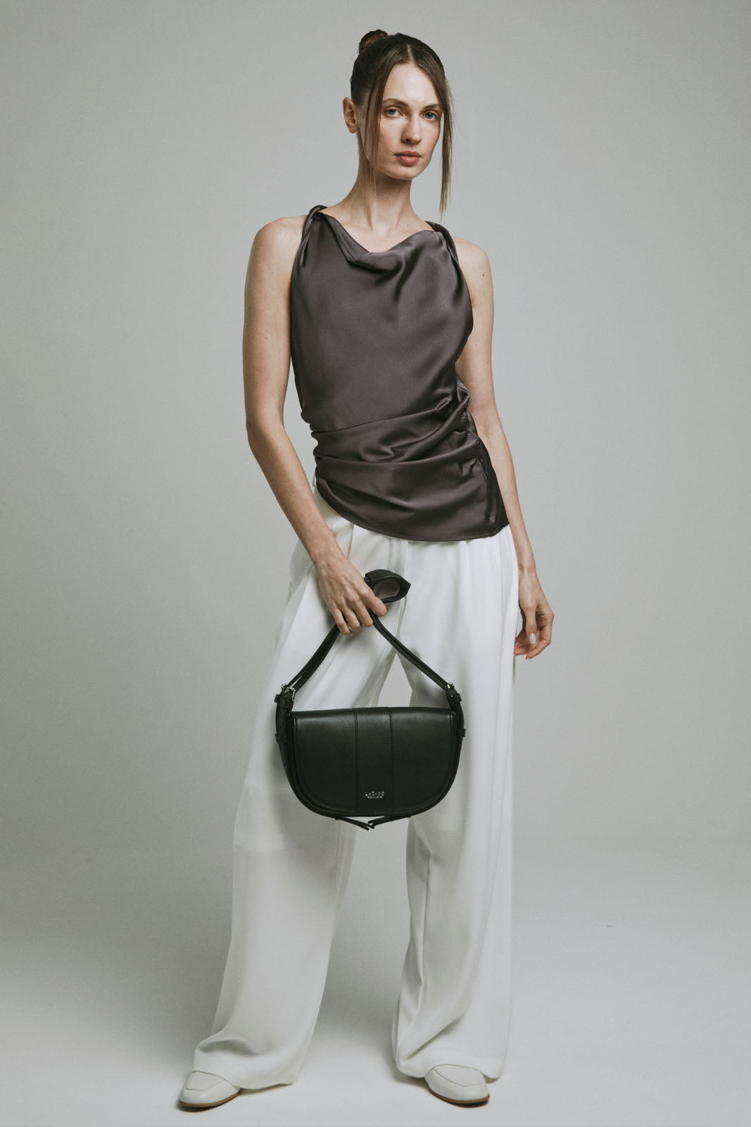 A model carries a sophisticated black leather shoulder bag, showcasing its sophisticated design. The model confidently displays the bag's size and craftsmanship while exuding a sense of style and elegance.