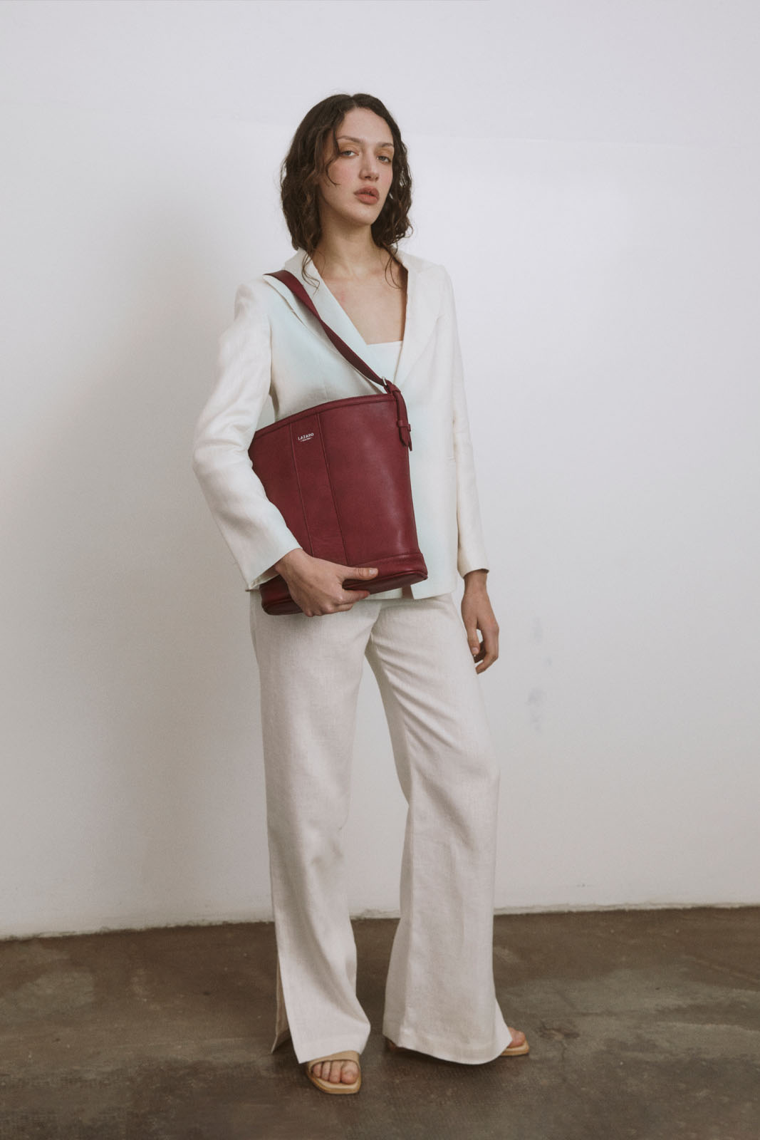 A model carries a sophisticated burgundy leather tote bag, showcasing its sophisticated design. The model confidently displays the bag's size and craftsmanship while exuding a sense of style and elegance.