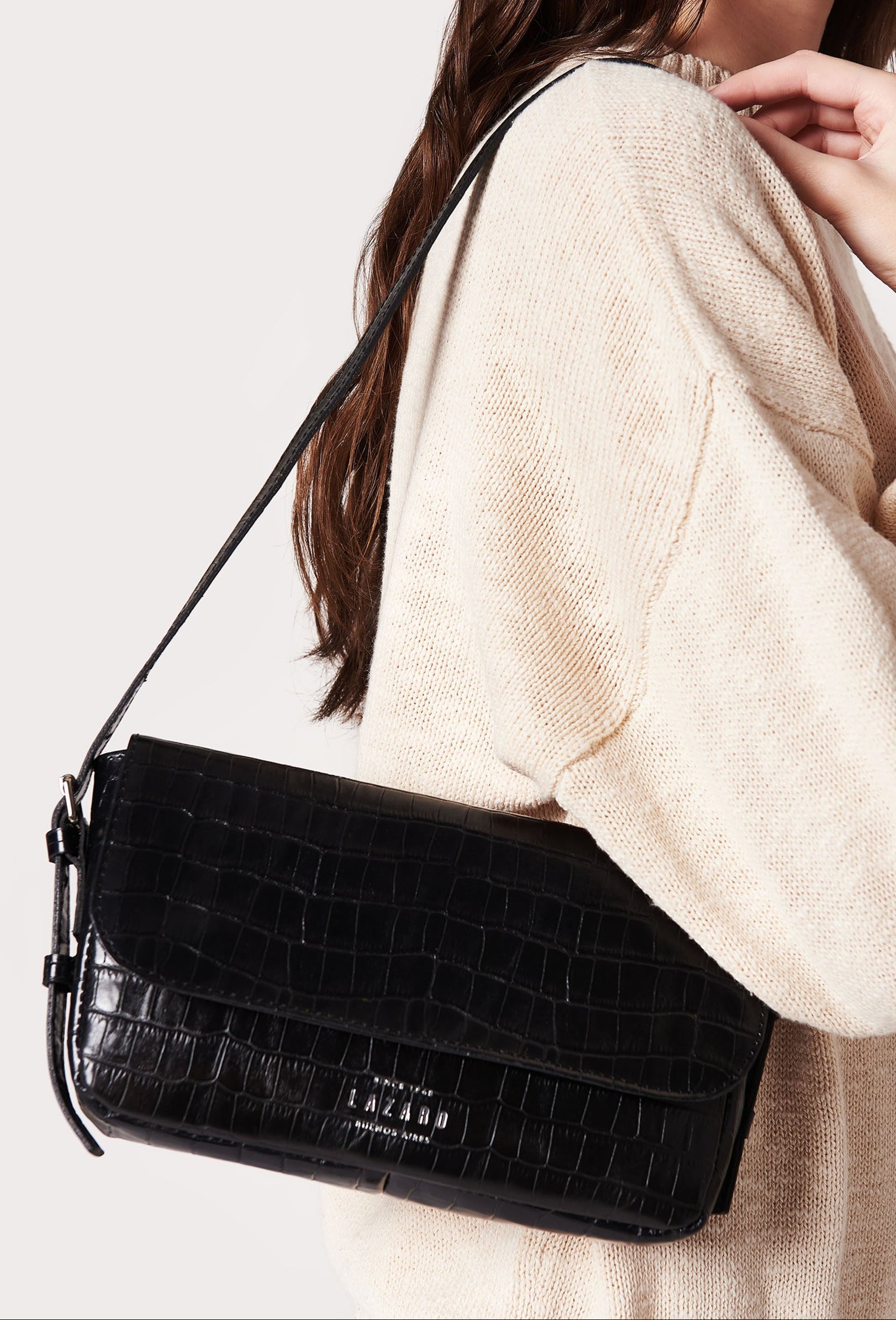 Black crocodile-patterned handbag worn by a person in a beige sweater on a white background