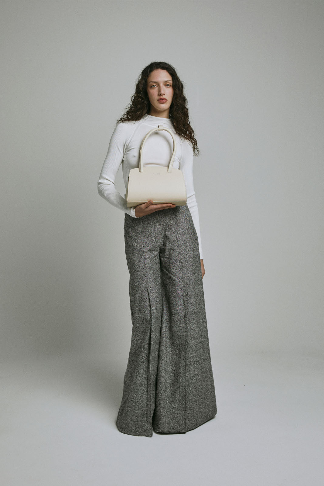 A model carries a sophisticated off white leather shoulder bag, showcasing its sophisticated design. The model confidently displays the bag's size and craftsmanship while exuding a sense of style and elegance.