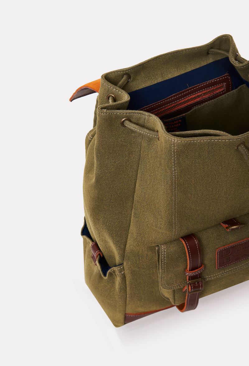 Partial photo of a Olive Canvas Backpack with leather details, a main compartment and distressed antiqued bronze fittings.