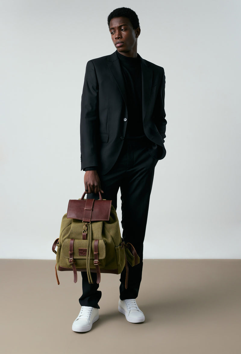 A model carries a sophisticated olive canvas backpack, showcasing its luxurious design. The bag features coffee leather details, adding to its elegant appeal. The model confidently displays the bag's size and craftsmanship while exuding a sense of style and sophistication.