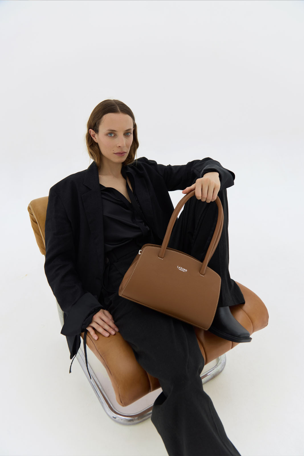 A model carries a sophisticated tan leather shoulder bag, showcasing its sophisticated design. The model confidently displays the bag's size and craftsmanship while exuding a sense of style and elegance.