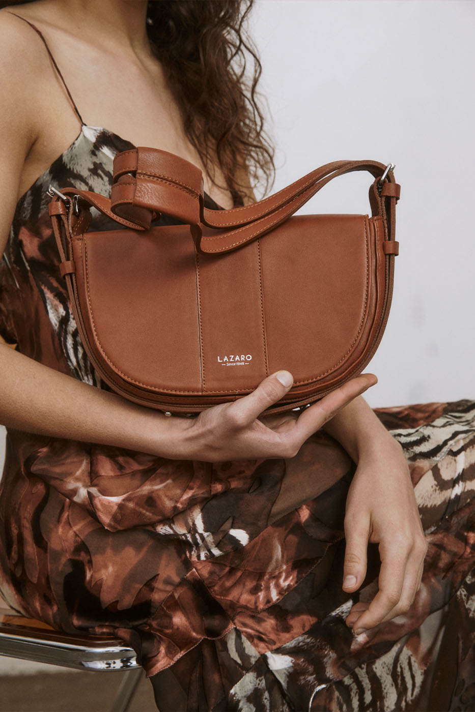 A model carries a sophisticated tan leather shoulder bag, showcasing its sophisticated design. The model confidently displays the bag's size and craftsmanship while exuding a sense of style and elegance.