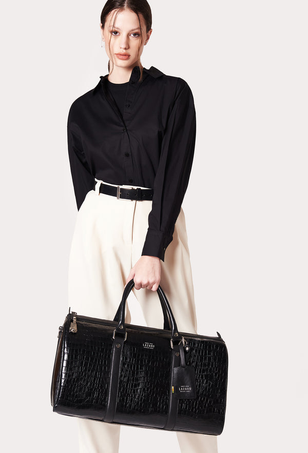 A model carries a sophisticated black croco leather duffel bag, showcasing its luxurious design. The bag features a lock closure, adding to its elegant appeal. The model confidently displays the bag's size and craftsmanship while exuding a sense of style and sophistication.