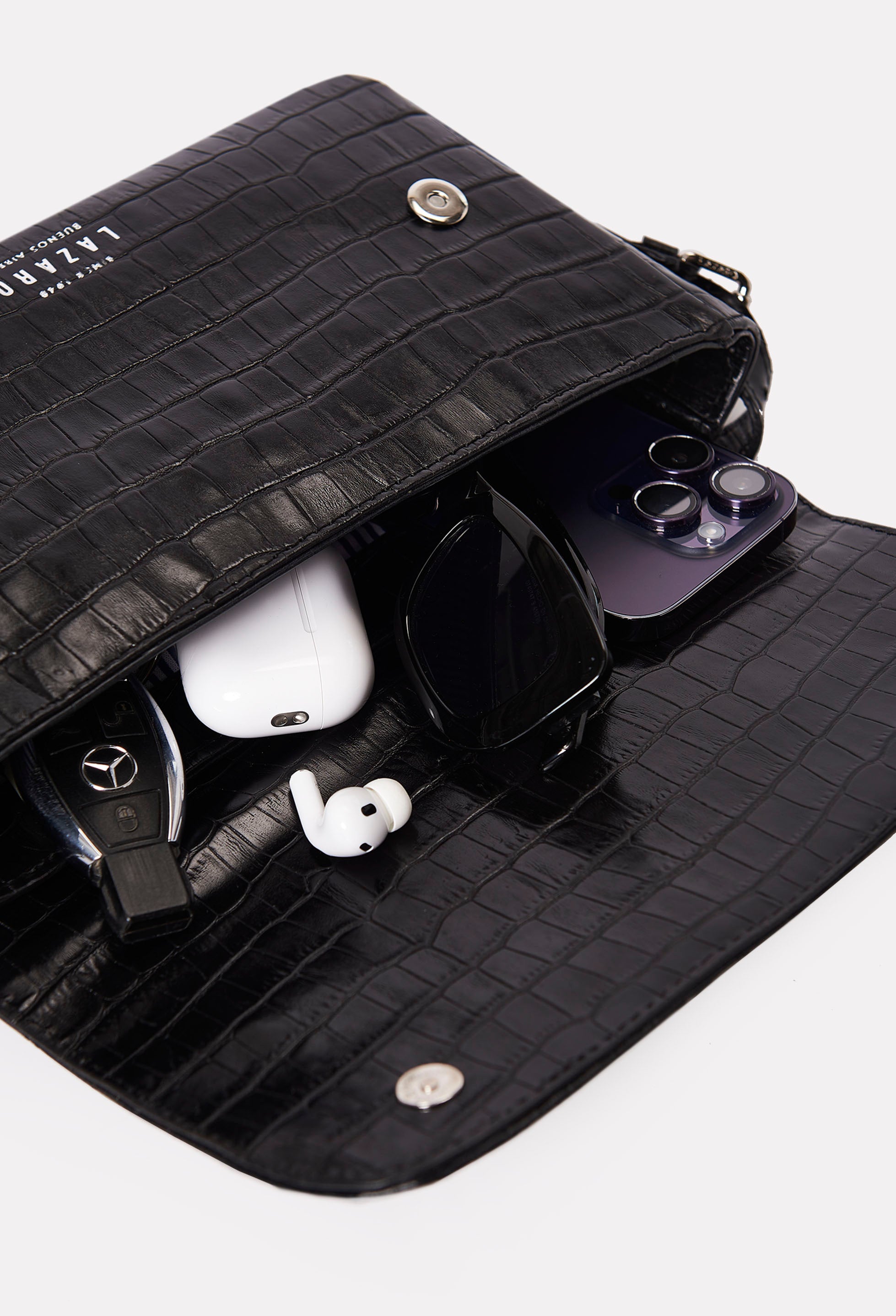 Interior of a Black Croco Leather Shoulder Flap Bag Gwen that shows the bag packed with a cell phone, sunglasses, earphones and car keys.