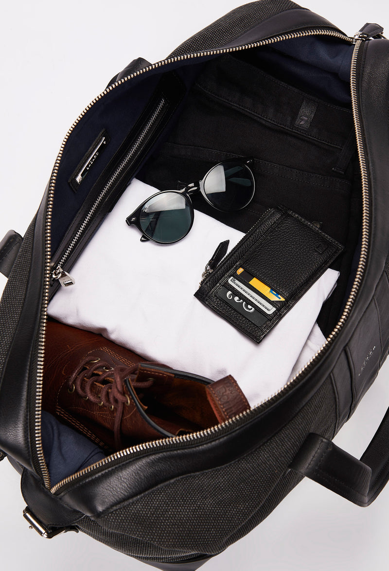 Interior of a Black Large Canvas Duffel Bag packed with a Lazaro cardholder, clothes, sunglasses and a pair of shoes.
