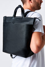 A model carries a sophisticated black leather tote style backpack, showcasing its sophisticated design. The bag features external and internal multifunctional zippered pockets, adding to its elegant appeal. The model confidently displays the bag's size and craftsmanship while exuding a sense of style and elegance.