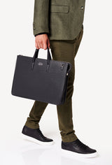A model carries a sophisticated black leather slim briefcase, showcasing its sophisticated design. The bag features a detachable shoulder strap, adding to its elegant appeal. The model confidently displays the bag's size and craftsmanship while exuding a sense of style and elegance.