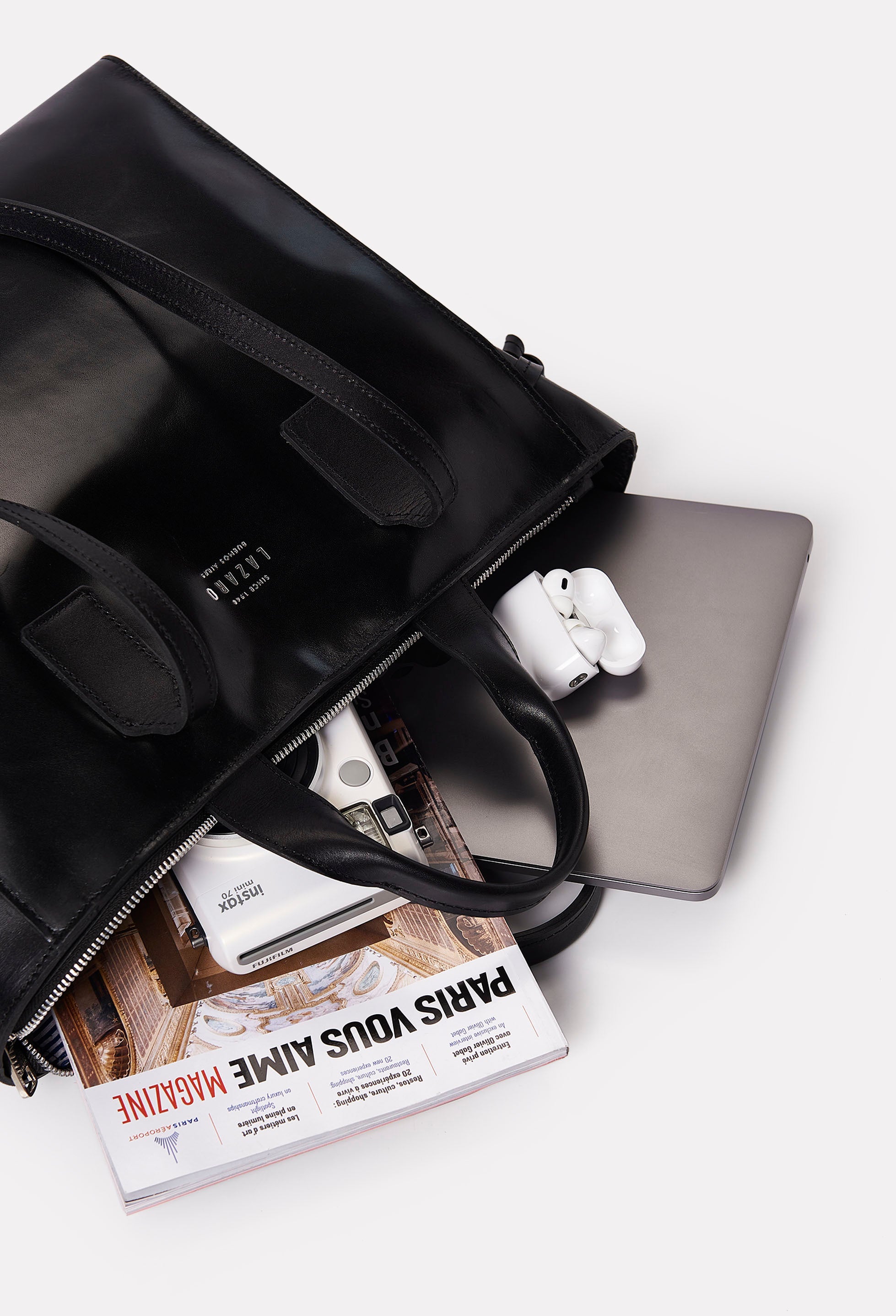 Interior of a Black Leather Tote Bag Lambro that shows the bag packed with a computer, a camera, a magazine and a earphones.