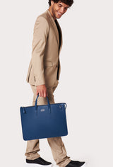 A model carries a sophisticated blue leather slim briefcase, showcasing its sophisticated design. The bag features a detachable shoulder strap, adding to its elegant appeal. The model confidently displays the bag's size and craftsmanship while exuding a sense of style and elegance.