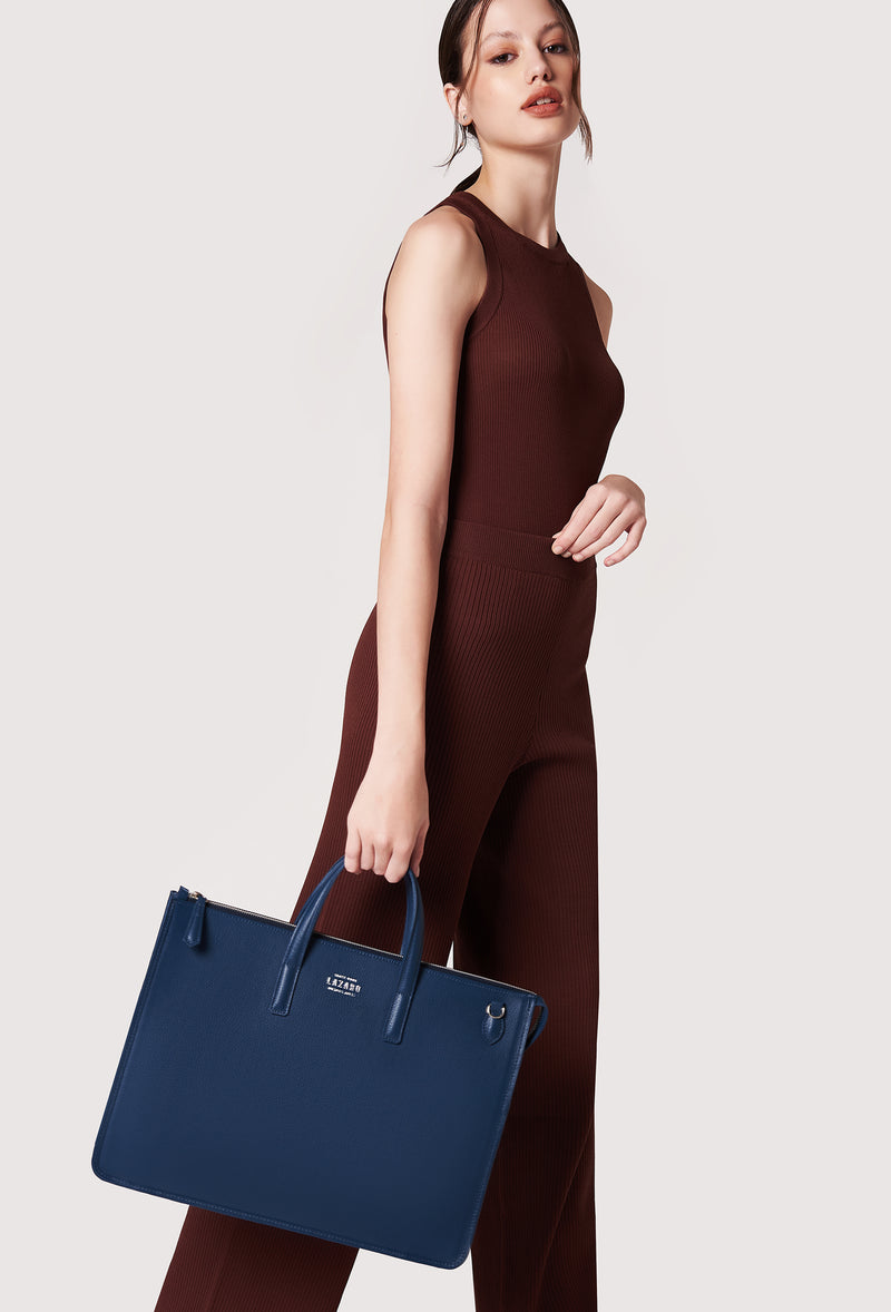 A model carries a sophisticated blue leather slim briefcase, showcasing its sophisticated design. The bag features a detachable shoulder strap, adding to its elegant appeal. The model confidently displays the bag's size and craftsmanship while exuding a sense of style and elegance.