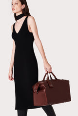 A model carries a sophisticated coffee leather duffel bag, showcasing its luxurious design. The bag features a unique needlework on its sides, adding to its elegant appeal. The model confidently displays the bag's size and craftsmanship while exuding a sense of style and sophistication.