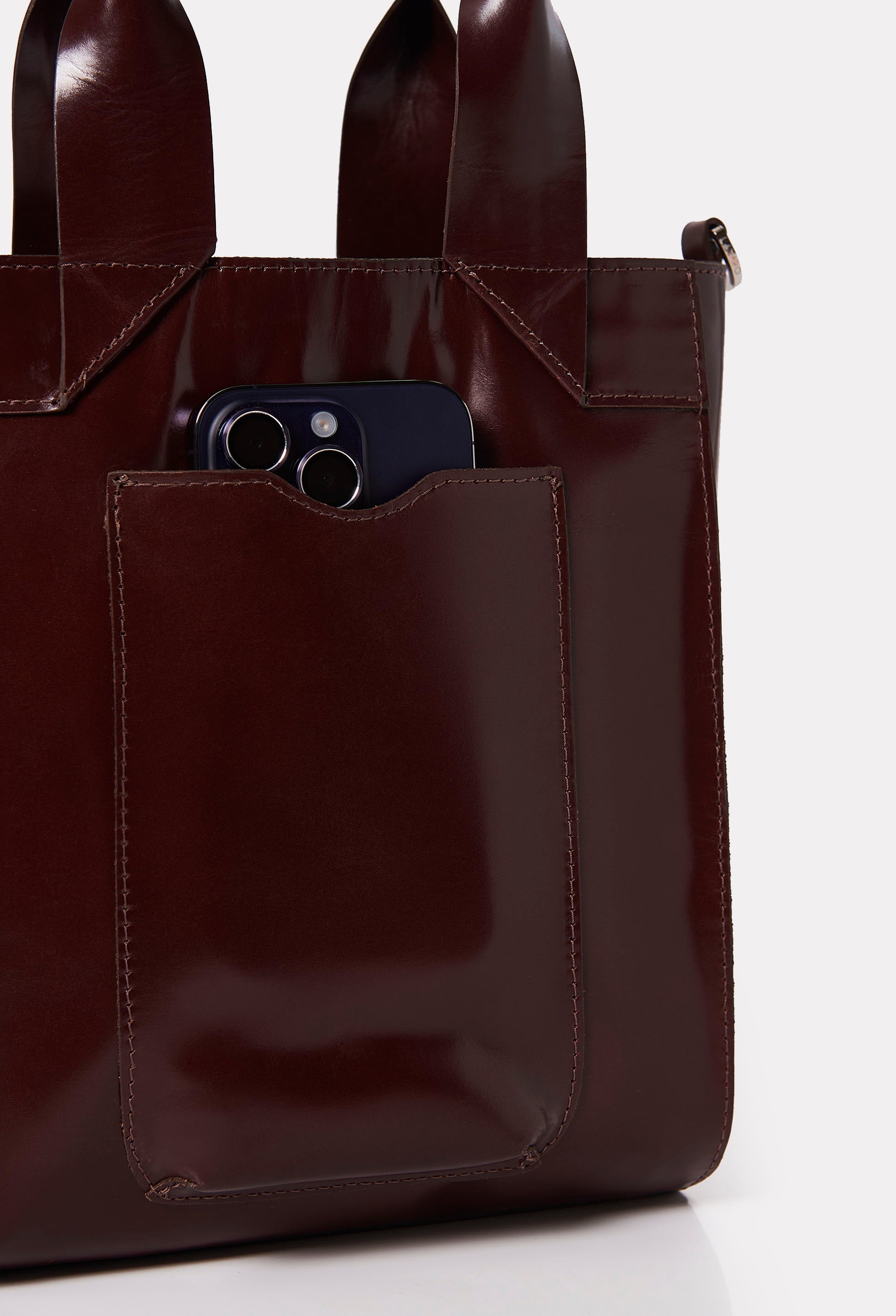 Partial photo of a Coffee Leather Mini Tote Bag Lambro with an external cell phone holder pocket.