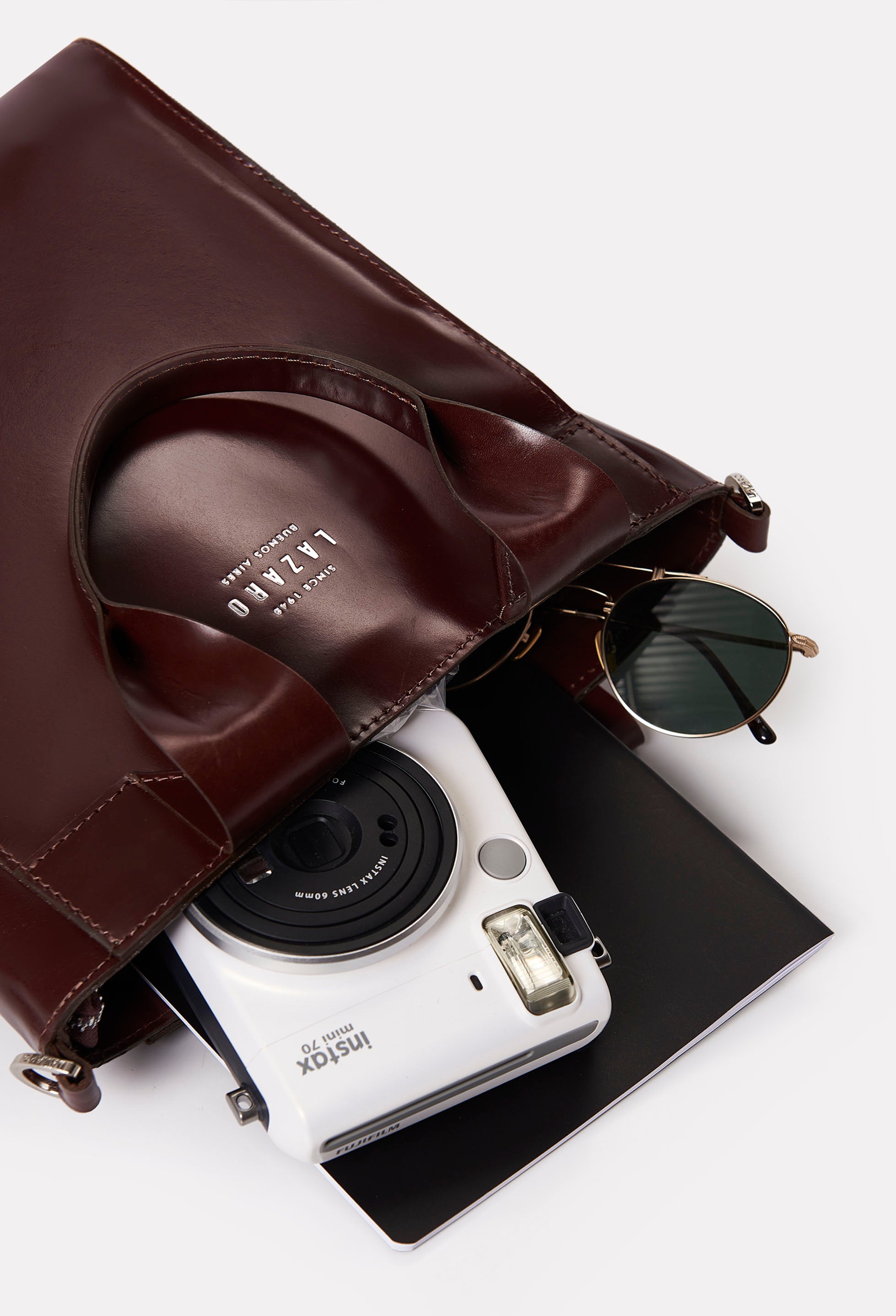 Interior of a Coffee Leather Mini Tote Bag Lambro that shows the bag packed with a camera, sunglasses and a notebook.