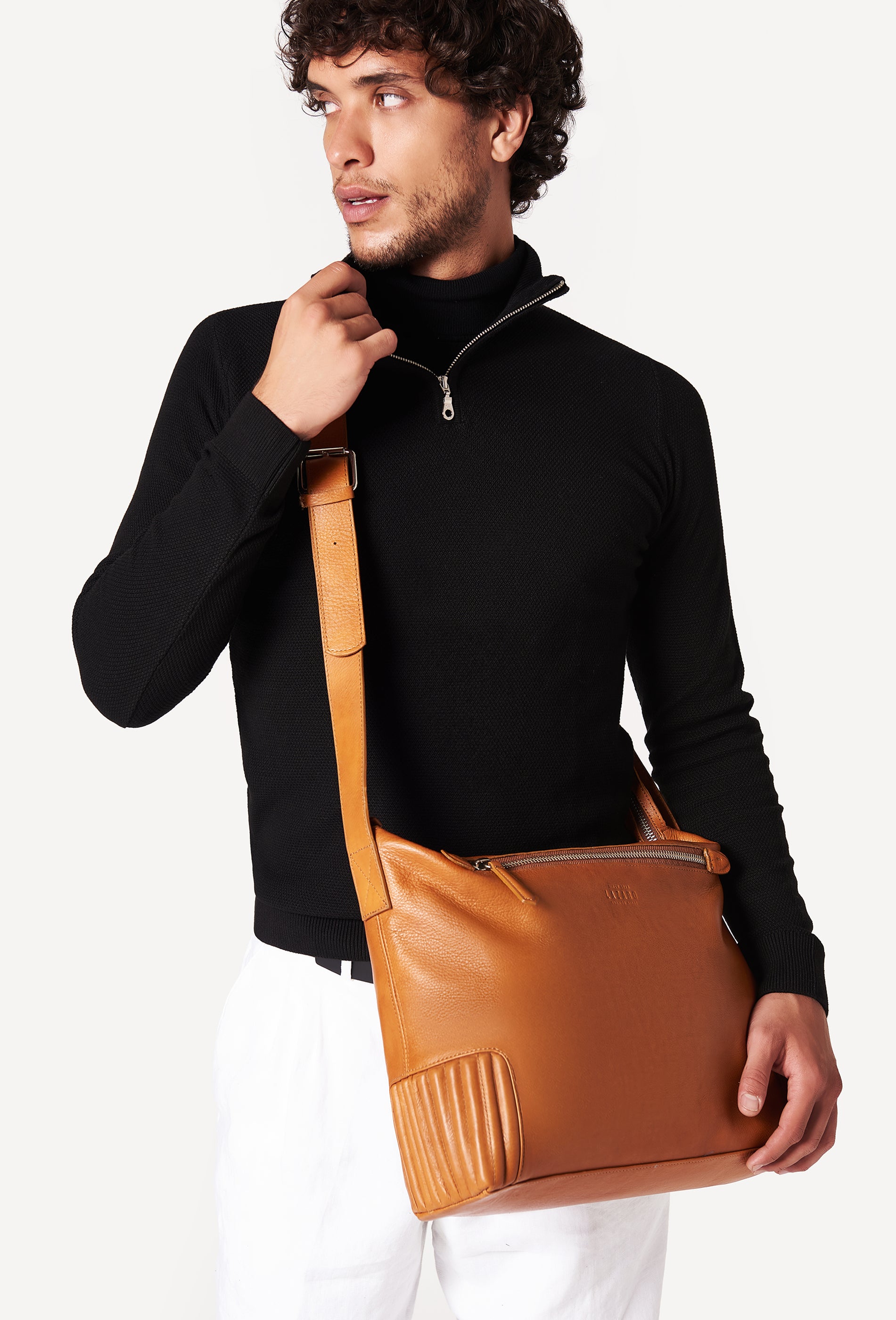 A model carries a sophisticated tan leather crossbody messenger, showcasing its sophisticated design. The bag features unique needlework on its side, adding to its elegant appeal. The model confidently displays the bag's size and craftsmanship while exuding a sense of style and elegance.