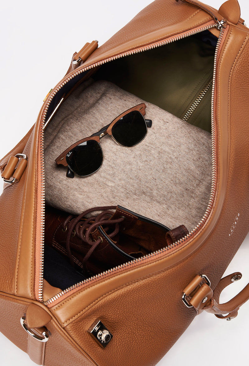Interior of a Tan Leather Duffel Bag with lock closure packed with clothes, sunglasses and a pair of shoes.