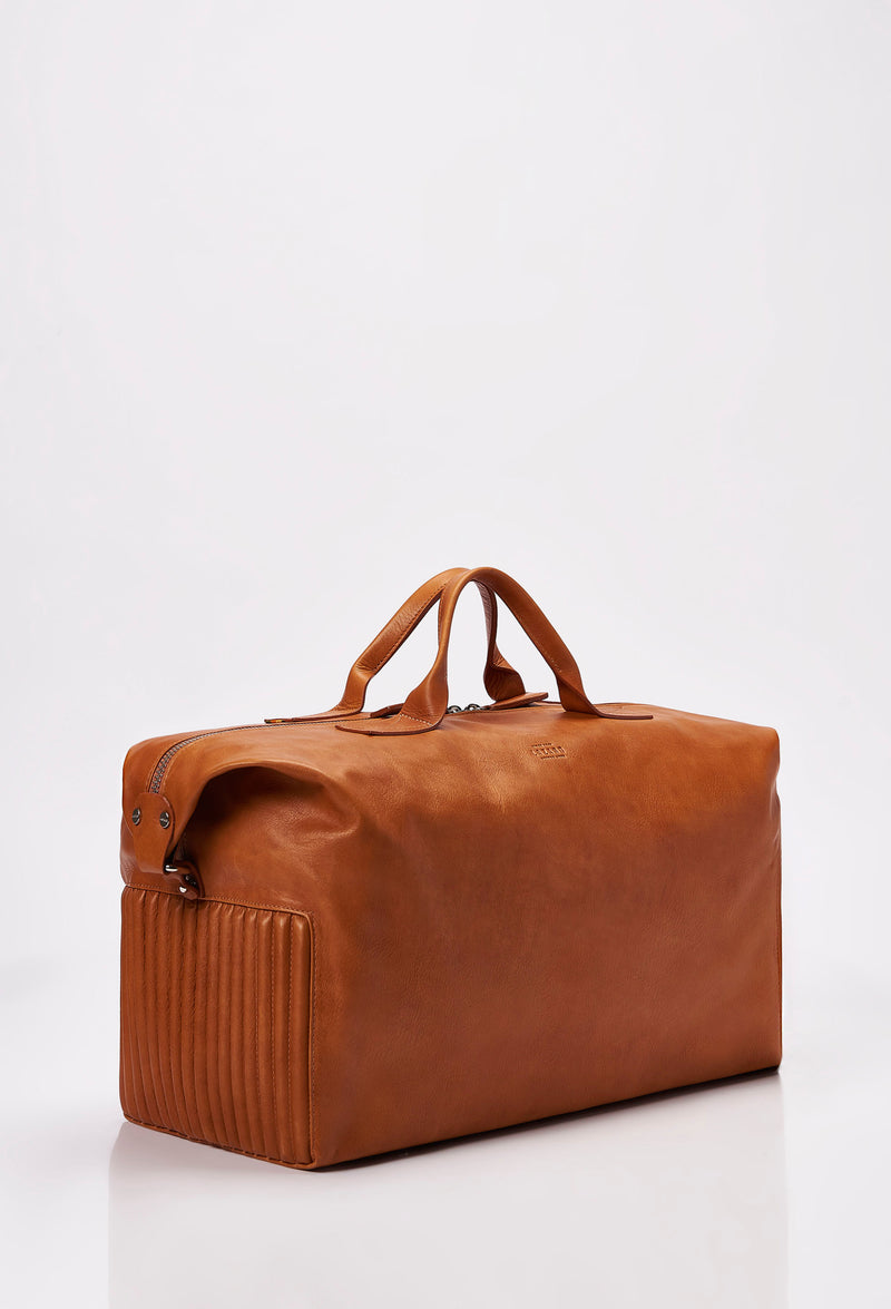 Side of a Tan Leather Duffel Bag with side needlework, Lazaro logo and a main zippered compartment.