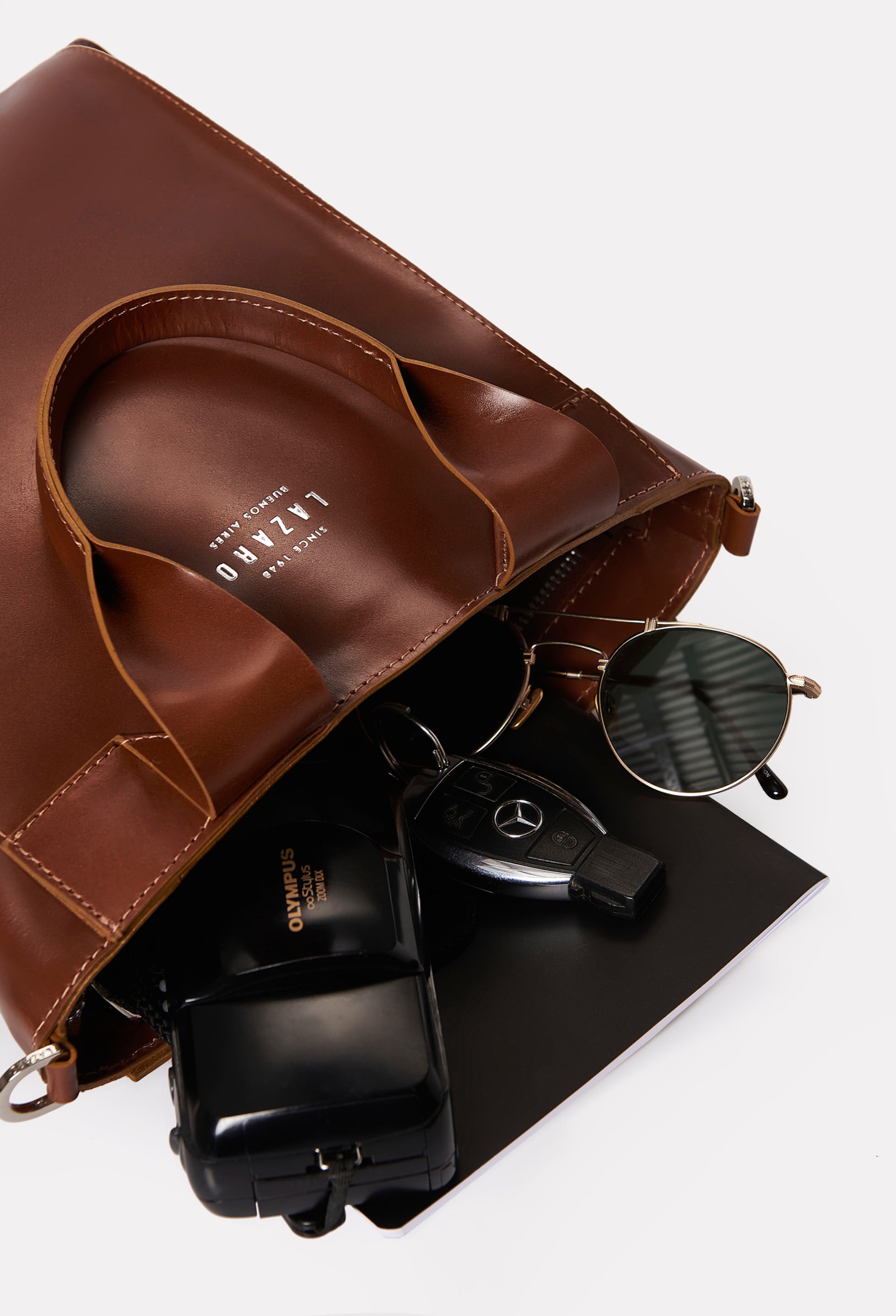Interior of a Tan Leather Mini Tote Bag Lambro that shows the bag packed with a camera, sunglasses, car keys and a notebook.